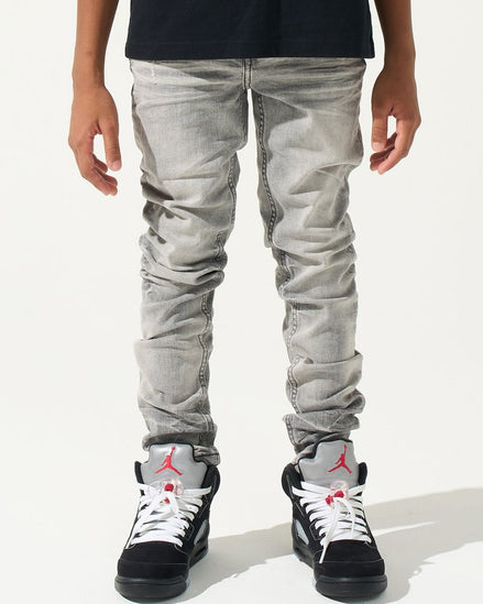 Person wearing light gray jeans and black sneakers with red accents on a white background