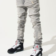 Person wearing light gray jeans and black sneakers with red accents on a white background