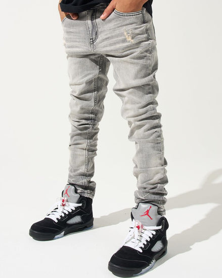 Person wearing light gray jeans and black sneakers with red accents on a white background