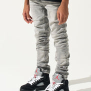 Person wearing light gray jeans and black sneakers with red accents on a white background
