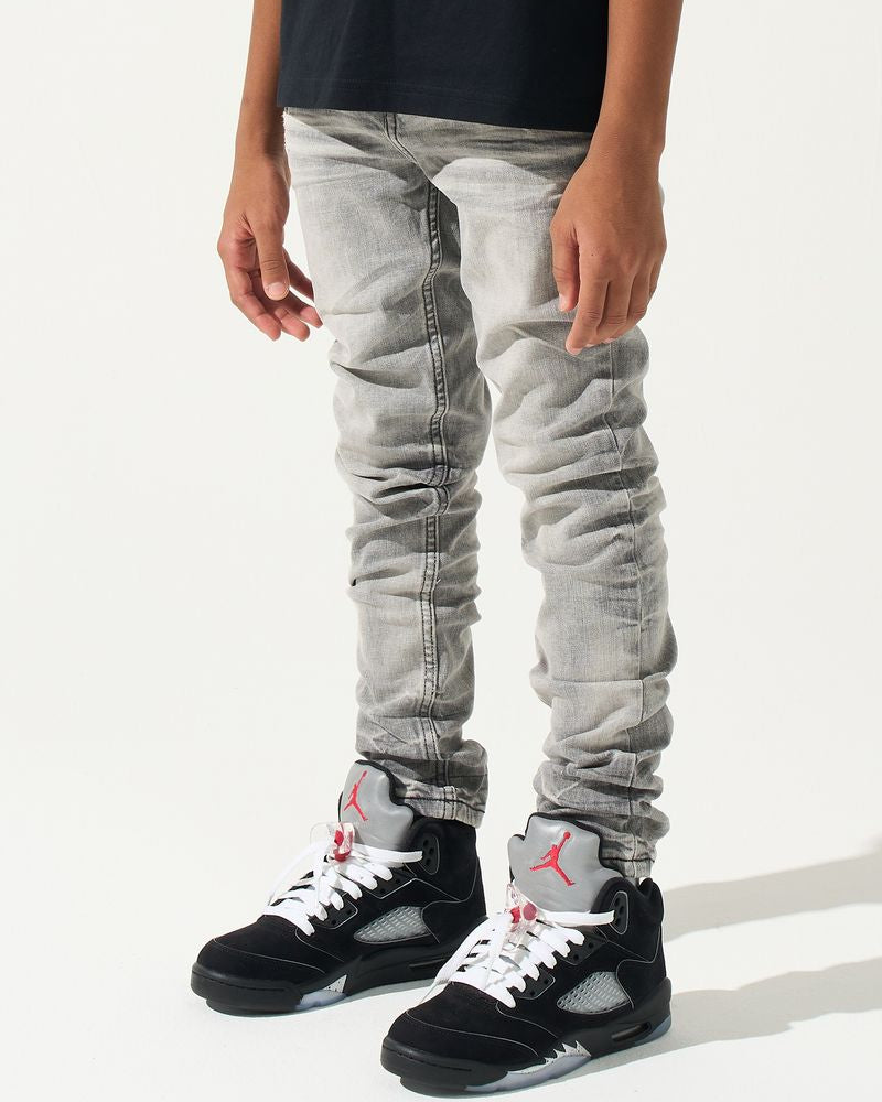 Person wearing light gray jeans and black sneakers with red accents on a white background