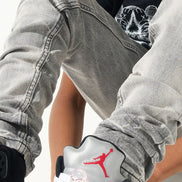 Person wearing gray pants and a black shirt with a red logo, sitting on a white background.