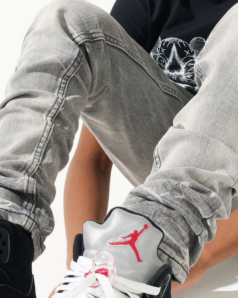 Person wearing gray pants and a black shirt with a red logo, sitting on a white background.