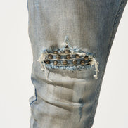 Close-up of distressed denim jeans with a decorative element on a light gray background