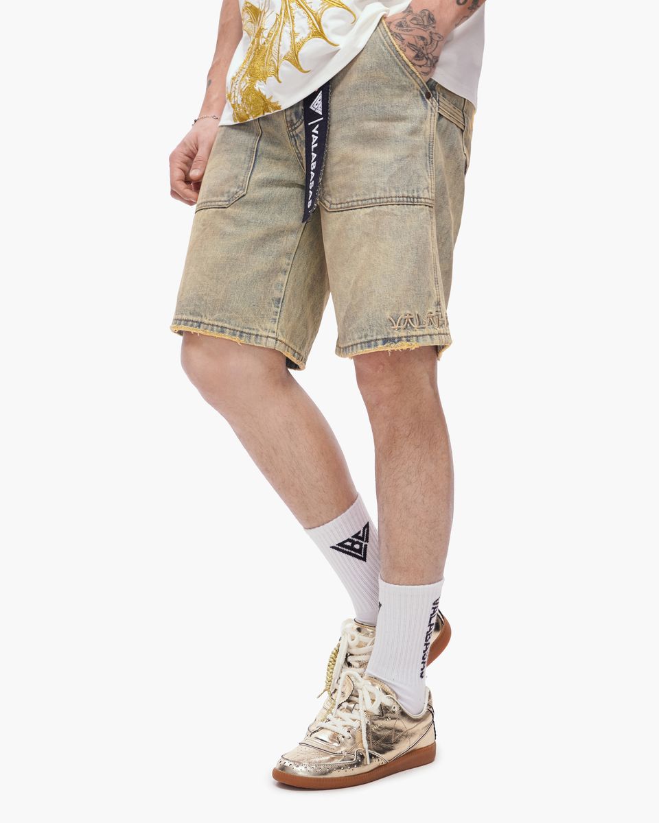 Person wearing beige shorts, white socks with a logo, and sneakers on a white background