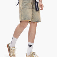 Person wearing light-colored denim shorts with a brand logo, white socks, and gold sneakers on a white background.