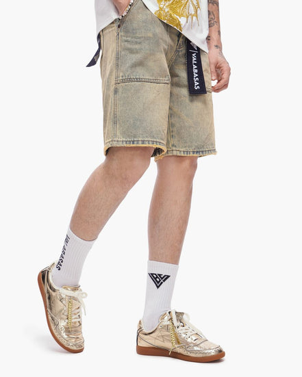 Person wearing light-colored denim shorts with a brand logo, white socks, and gold sneakers on a white background.