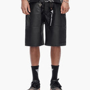 Person wearing black leather shorts with visible branding on a white background