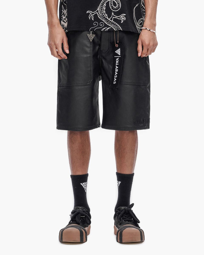 Person wearing black leather shorts with visible branding on a white background