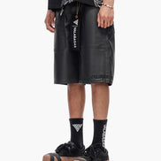 Person wearing black leather shorts with visible branding on a white background