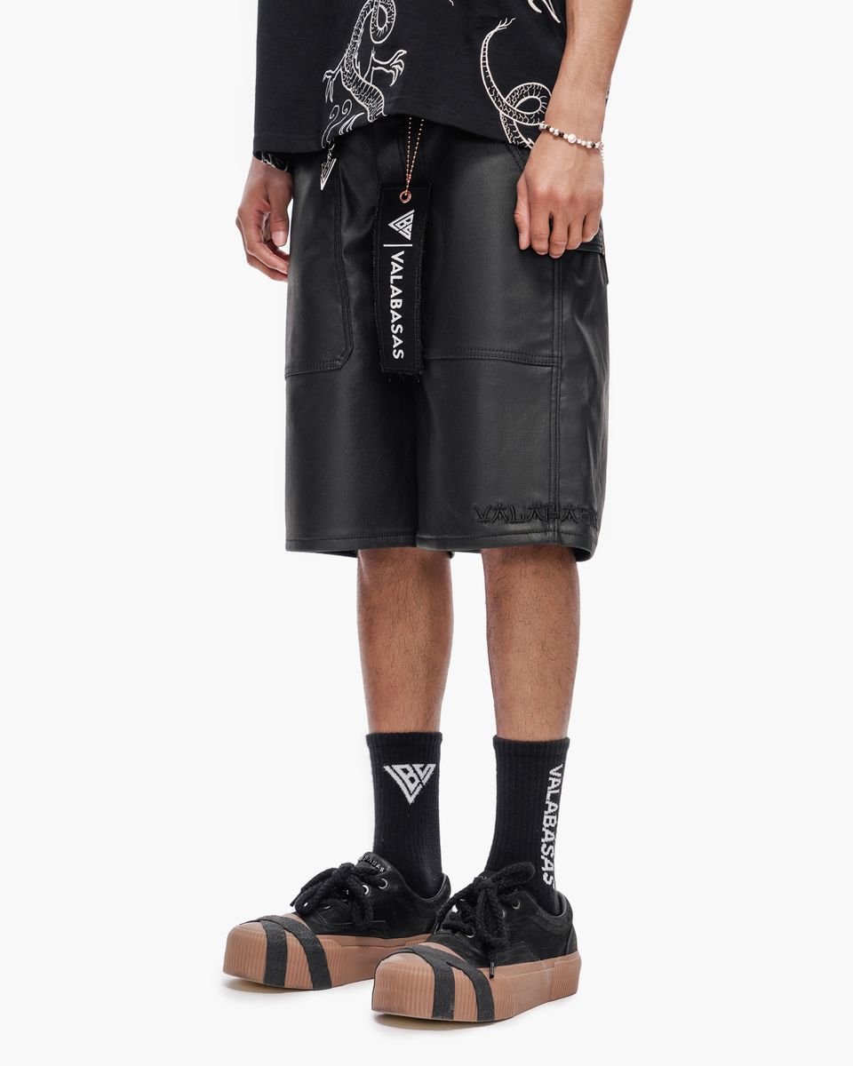 Person wearing black leather shorts with visible branding on a white background