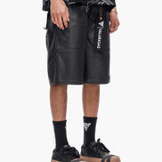 Person wearing black leather shorts with a brand logo on a white background