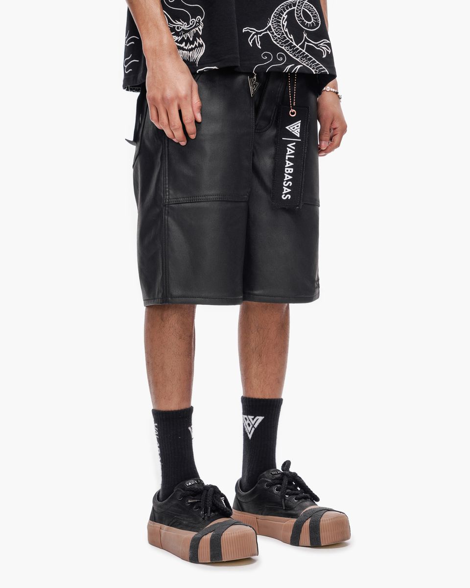 Person wearing black leather shorts with a brand logo on a white background