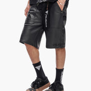 Person wearing black leather shorts with visible branding on a white background