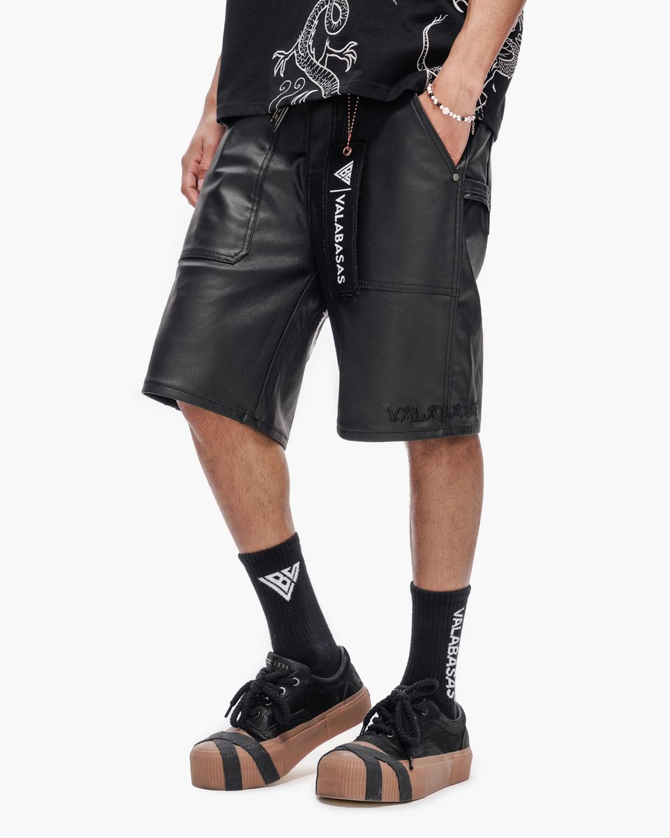 Person wearing black leather shorts with visible branding on a white background