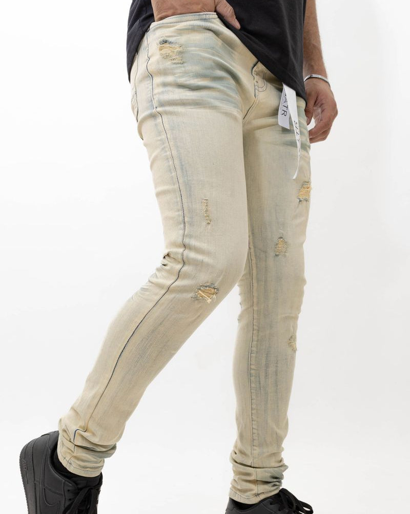 Person wearing light beige distressed jeans with black sneakers on a white background