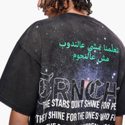 Person wearing a black t-shirt with text and graphics on the back, including Arabic script and a quote.