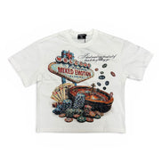 A white short-sleeve graphic t-shirt featuring a Las Vegas 'Welcome to Fabulous City of Mixed Emotion' sign surrounded by poker chips and a roulette wheel.