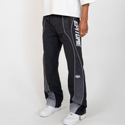 A person wearing black and gray athletic pants with white side stripes and white sneakers, shown from the waist down against a light gray studio background.
