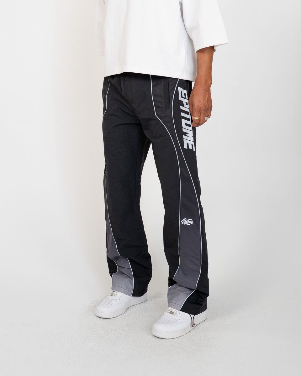 A person wearing black and gray athletic pants with white side stripes and white sneakers, shown from the waist down against a light gray studio background.