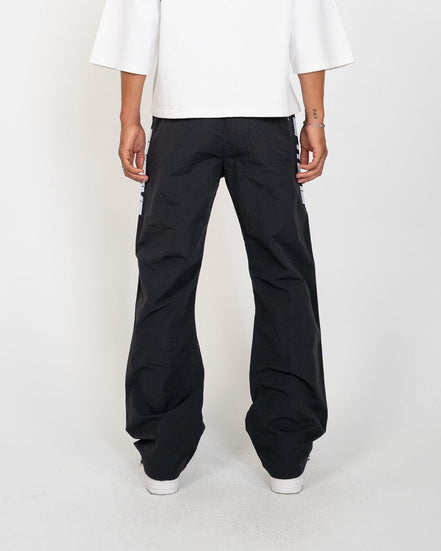 A person shown from the back wearing black wide-leg cargo pants with white sneakers and a white top, photographed against a plain light gray studio background.