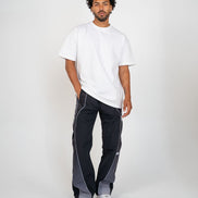 A man modeling a white short-sleeve t-shirt and dark gray side-panel track pants with white piping, paired with white sneakers, against a light gray studio background.