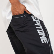 Close-up of a person wearing black athletic pants with large white 'EPITOME' lettering down the side and a white t-shirt, with one hand in the pocket.