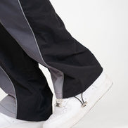 Close-up of a person's legs wearing black and gray wide-leg pants with white sneakers against a plain white background.