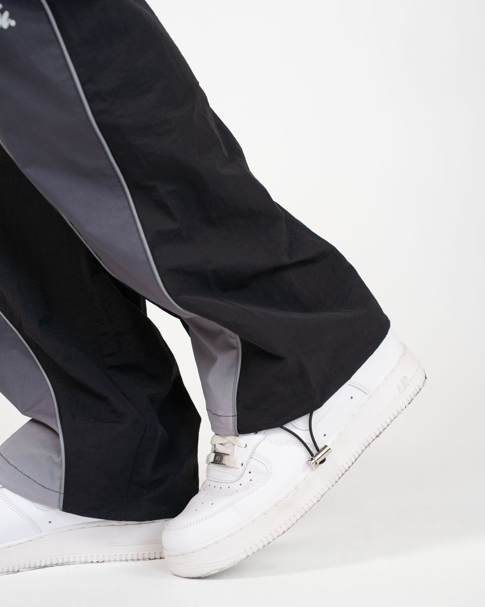Close-up of a person's legs wearing black and gray wide-leg pants with white sneakers against a plain white background.