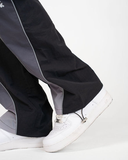Close-up of a person's legs wearing black and gray wide-leg pants with white sneakers against a plain white background.