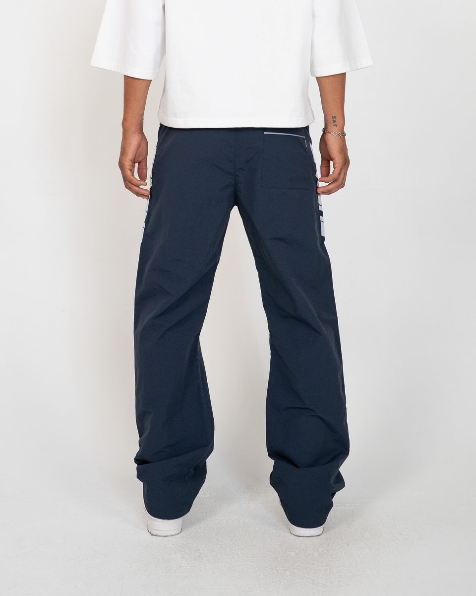 A person shown from the back wearing dark navy wide-leg pants with a white t-shirt and white sneakers, standing against a light gray studio background.