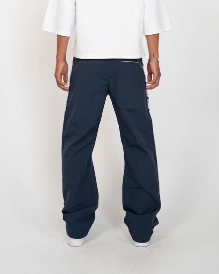 A person shown from the back wearing dark navy wide-leg pants with a white t-shirt and white sneakers, standing against a light gray studio background.