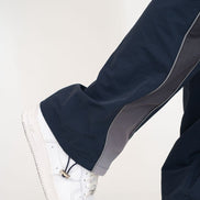 Close-up of a person's leg wearing navy blue pants with a gray side stripe and a white sneaker, shown against a plain light background.