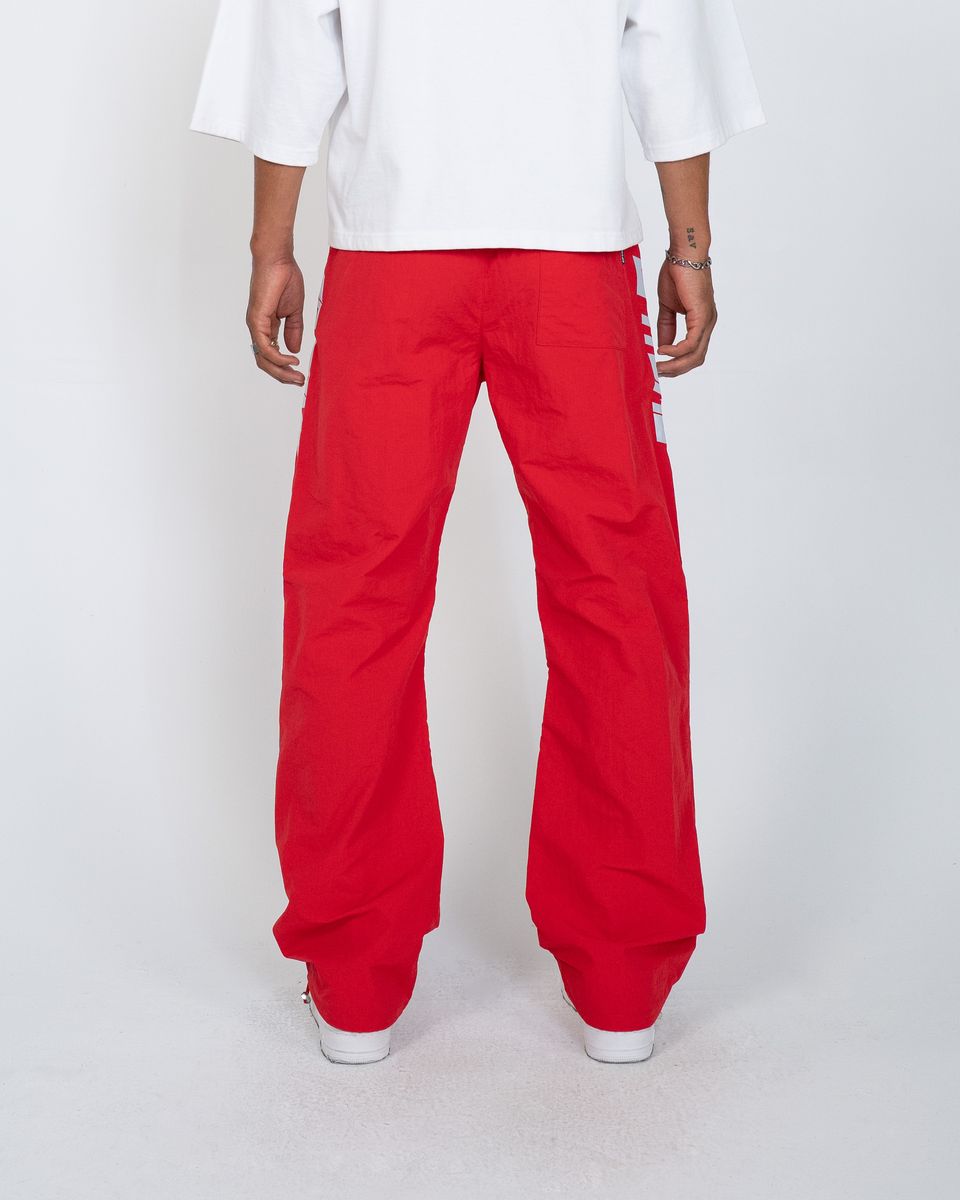 A person shown from the back wearing bright red wide-leg pants and a white T-shirt against a light gray studio background.
