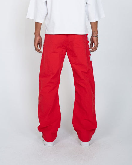 A person shown from the back wearing bright red wide-leg pants and a white T-shirt against a light gray studio background.