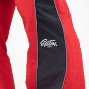 Close-up of red athletic pants with a wide black side stripe and a white 'EPTM.' logo on the thigh.