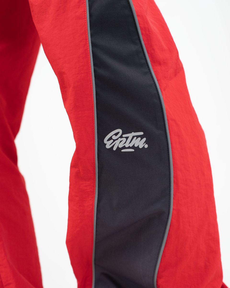 Close-up of red athletic pants with a wide black side stripe and a white 'EPTM.' logo on the thigh.