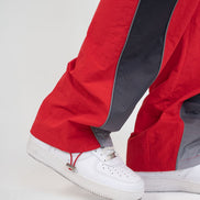 Close-up of a person's legs wearing red and dark gray wide-leg pants with white sneakers against a light gray studio background.