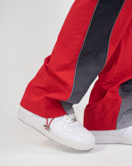 Close-up of a person's legs wearing red and dark gray wide-leg pants with white sneakers against a light gray studio background.