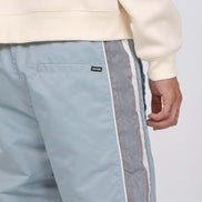 Light blue pants with white and gray side stripes worn with a beige sweatshirt on a light gray background