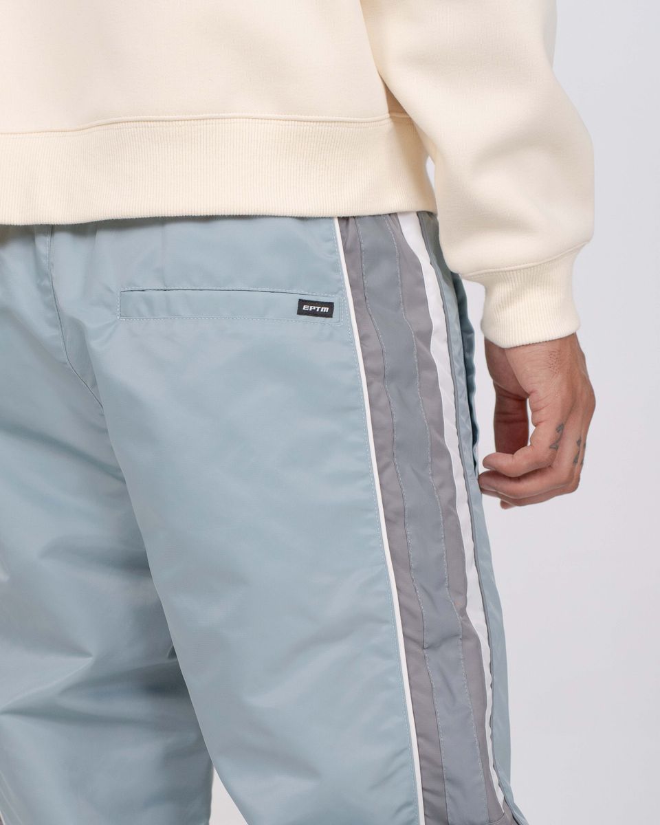 Light blue pants with white and gray side stripes worn with a beige sweatshirt on a light gray background