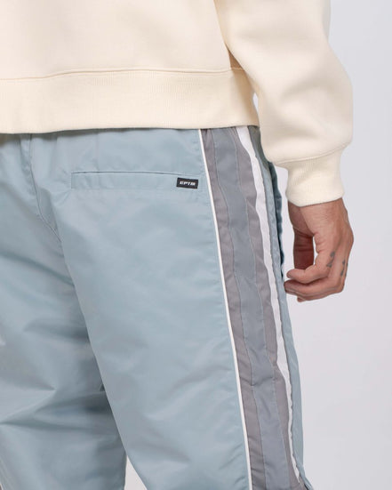 Light blue pants with white and gray side stripes worn with a beige sweatshirt on a light gray background