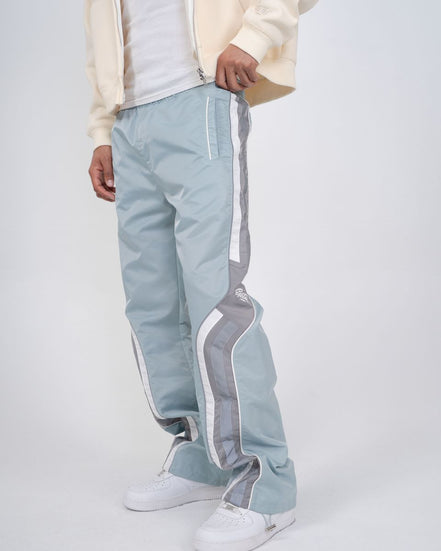 Light blue track pants with white stripes worn by a person on a light gray background