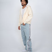 Man wearing a cream hoodie and light blue pants with white stripes on a white background