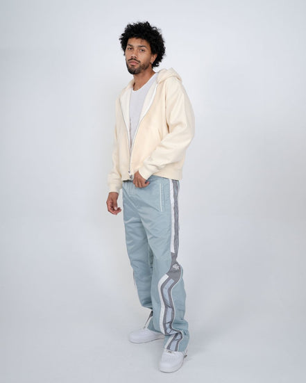 Man wearing a cream hoodie and light blue pants with white stripes on a white background