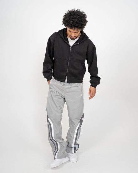 Person wearing a black hoodie and gray tracksuit with white stripes on a white background