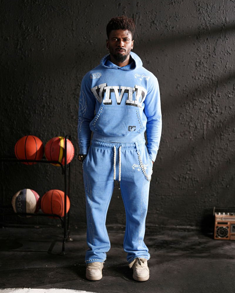 Person wearing a blue 'Vivid' tracksuit standing in front of a dark wall with basketballs on a rack.