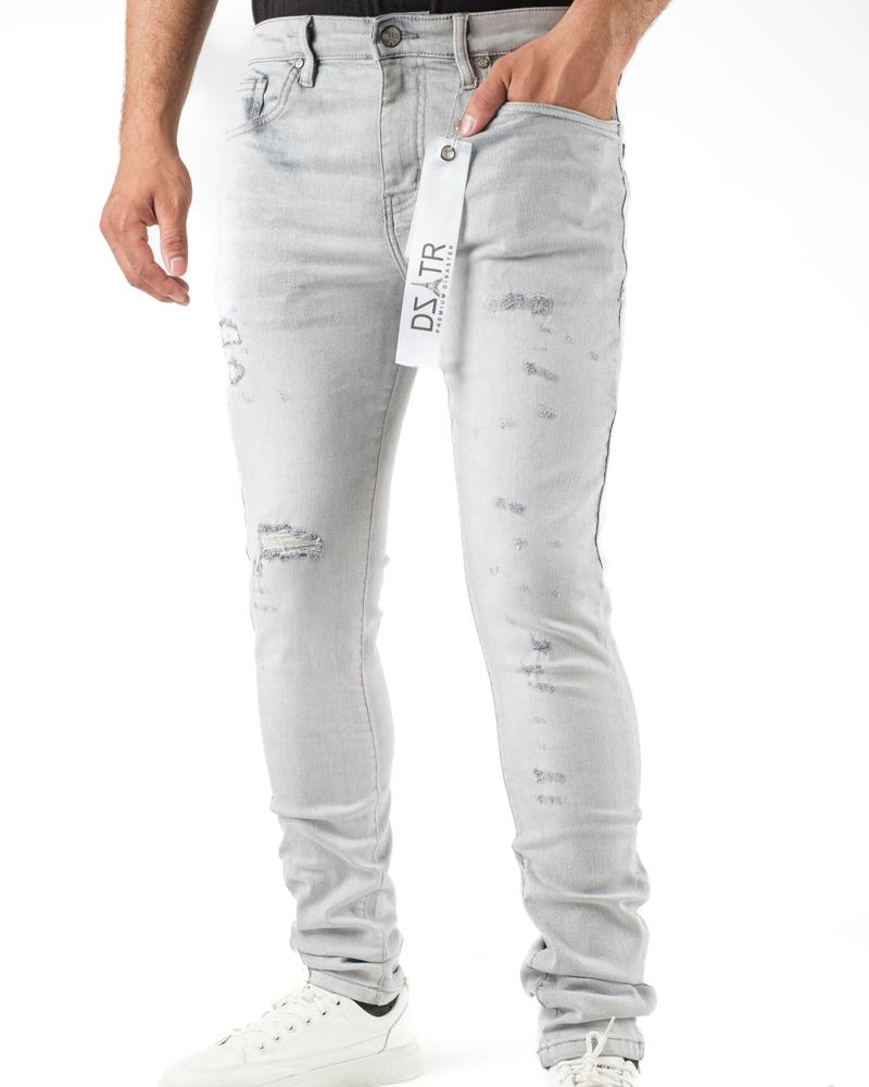Person wearing light gray distressed jeans with a brand tag on a white background