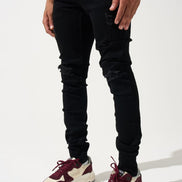Person wearing black ripped jeans and maroon and white sneakers on a white background