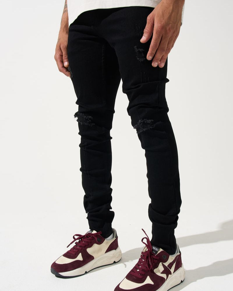 Person wearing black ripped jeans and maroon and white sneakers on a white background